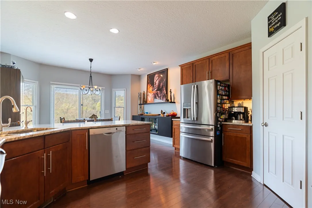 Kitchen with light stone countertops, a chandelier, appliances with stainless steel finishes, dark wood-style flooring, and a sink