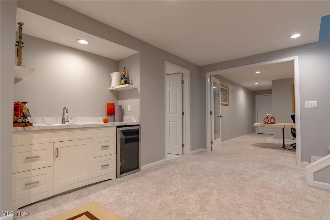 Kitchen with beverage cooler, light colored carpet, open shelves, a sink, and white cabinetry