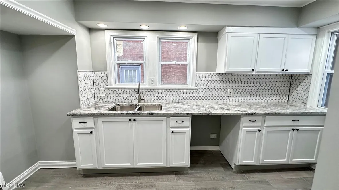 Kitchen featuring a sink, white cabinetry, decorative backsplash, and light stone countertops