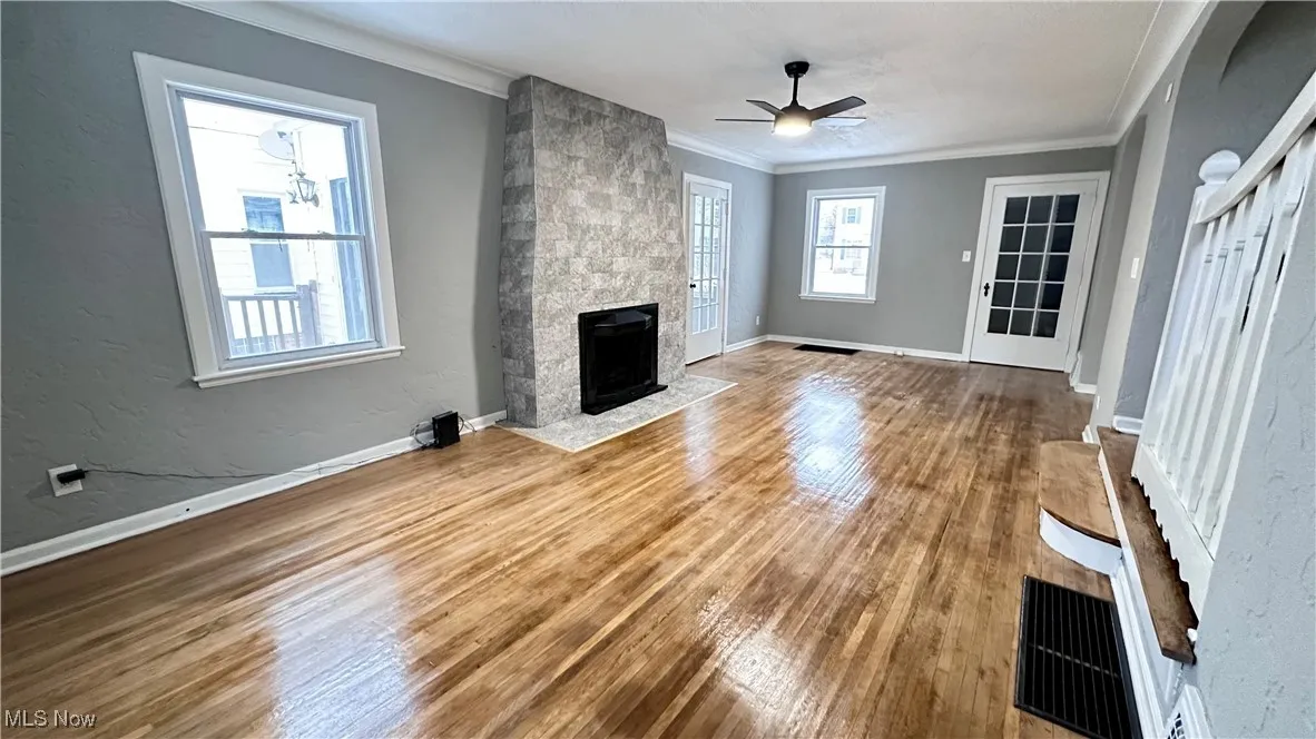 Unfurnished living room featuring ornamental molding, wood finished floors, baseboards, ceiling fan, and a large fireplace