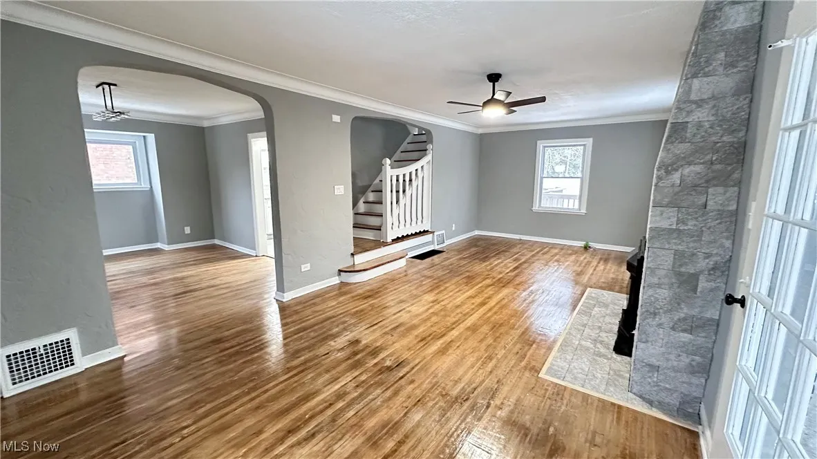 Unfurnished living room with arched walkways, a ceiling fan, visible vents, and wood finished floors