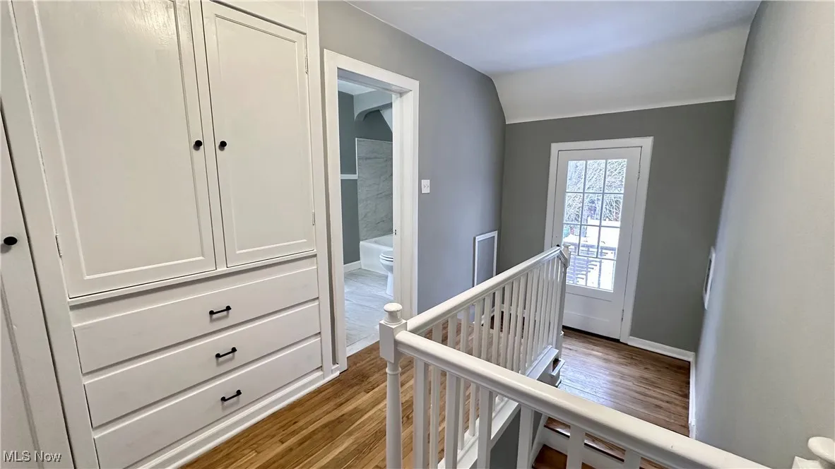 Hallway with baseboards, an upstairs landing, vaulted ceiling, and dark wood-type flooring