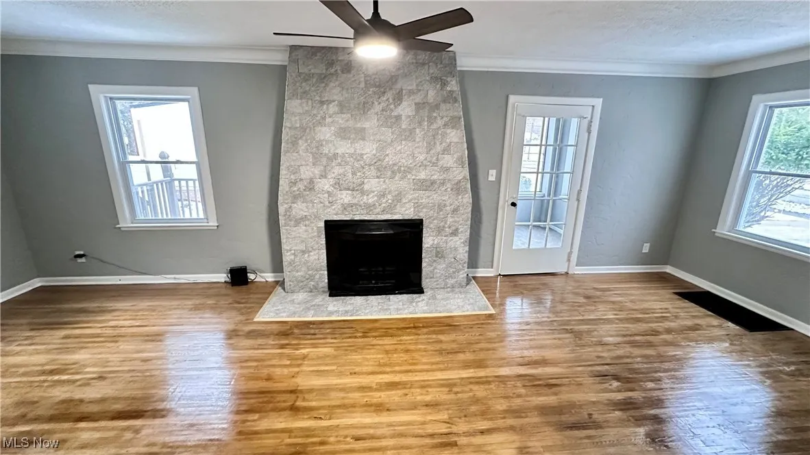Unfurnished living room with ornamental molding, a fireplace, a ceiling fan, and wood finished floors