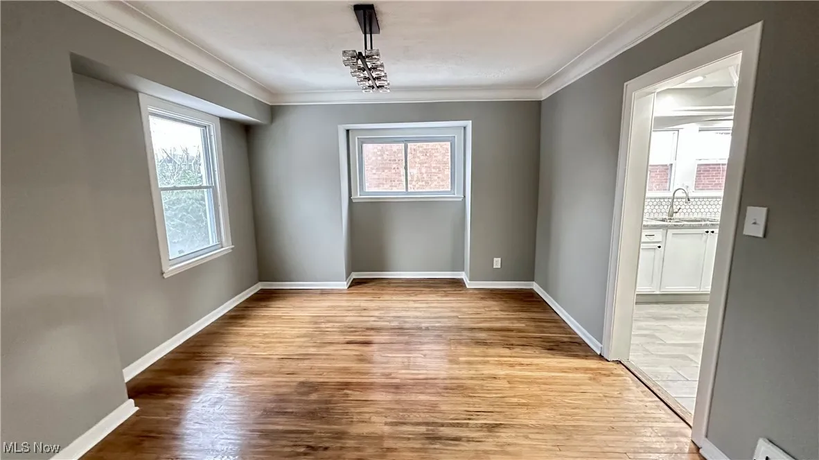 Unfurnished dining area with a sink, baseboards, crown molding, and wood finished floors