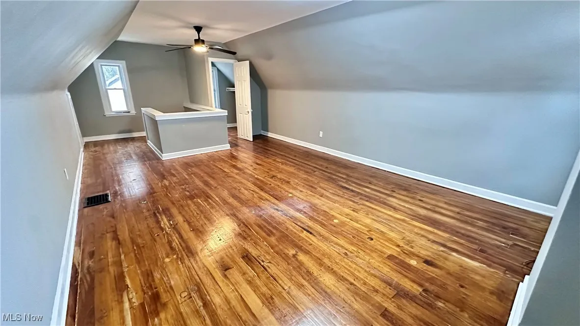 Bonus room featuring a ceiling fan, visible vents, vaulted ceiling, baseboards, and dark wood-style floors