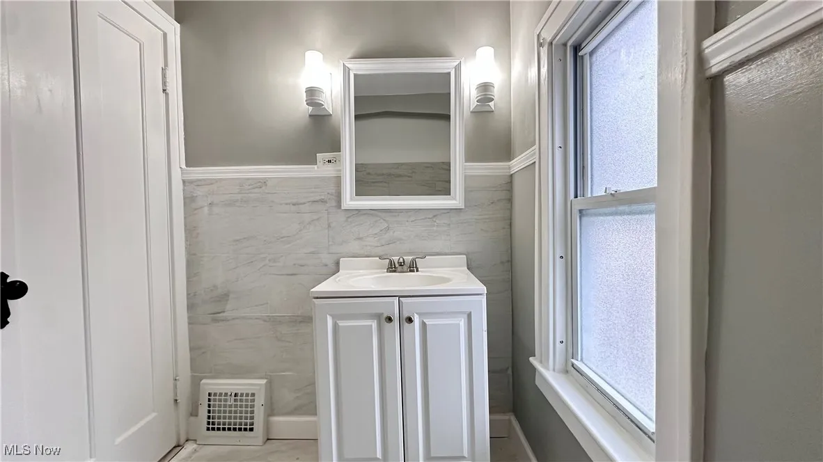 Bathroom featuring tile walls, visible vents, a wainscoted wall, and vanity
