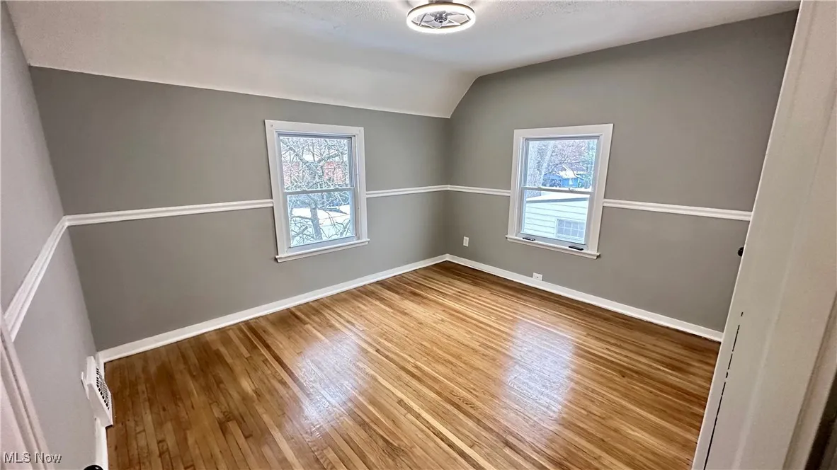 Unfurnished room with baseboards, wood finished floors, and lofted ceiling
