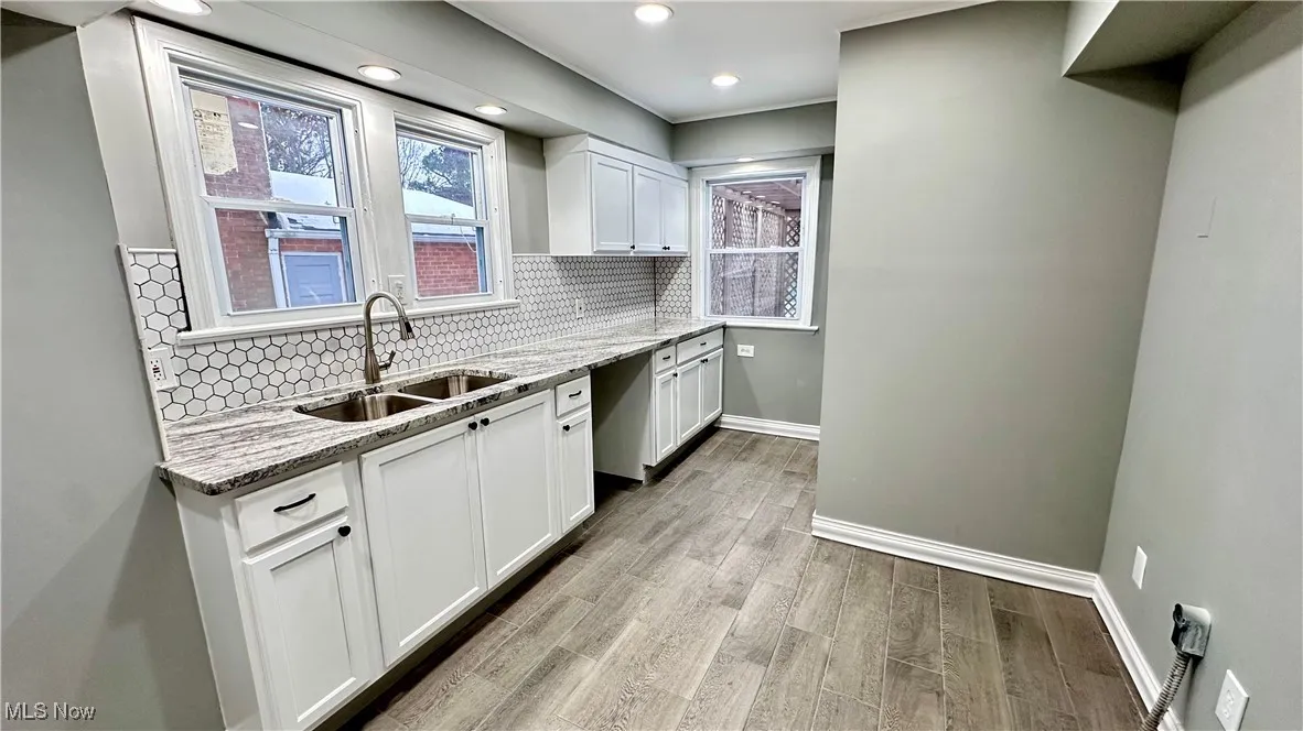 Kitchen with decorative backsplash, light stone countertops, baseboards, white cabinetry, and a sink