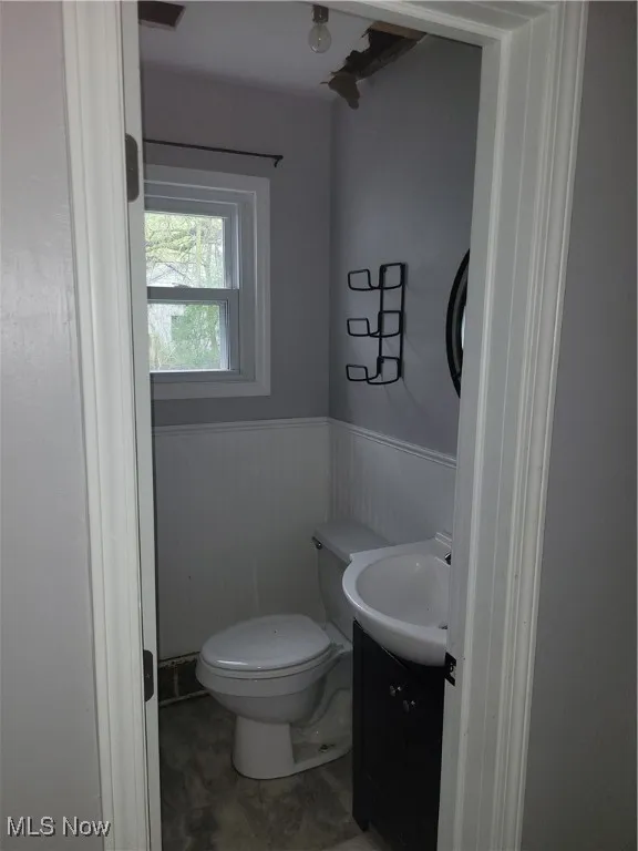 Half bath with vanity, toilet, and a wainscoted wall