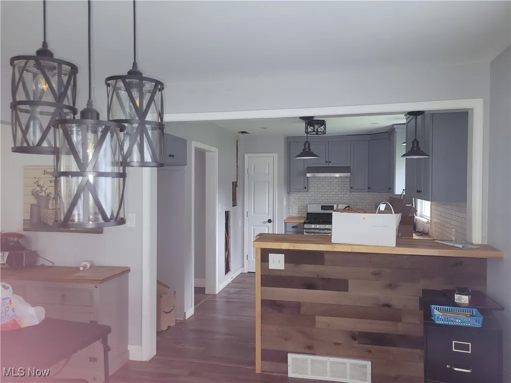 Kitchen with pendant lighting, stainless steel range with gas cooktop, tasteful backsplash, visible vents, and dark wood-style floors