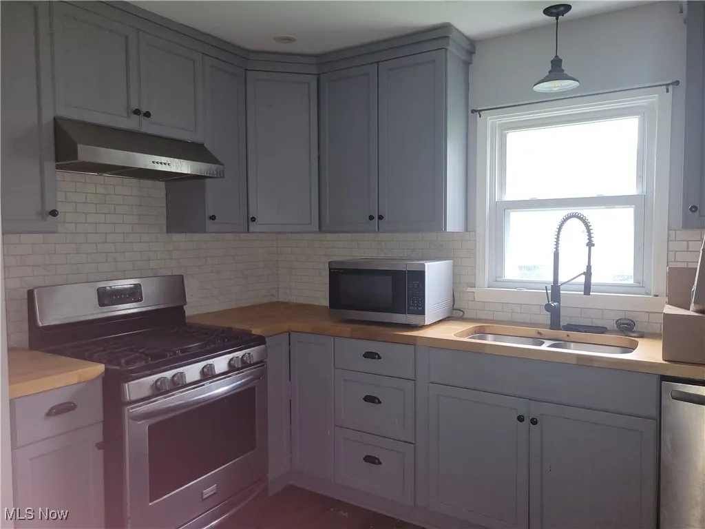 Kitchen with a sink, stainless steel appliances, backsplash, and under cabinet range hood