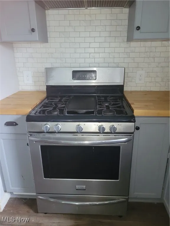 Kitchen featuring dark wood-style floors, decorative backsplash, butcher block counters, and gas range