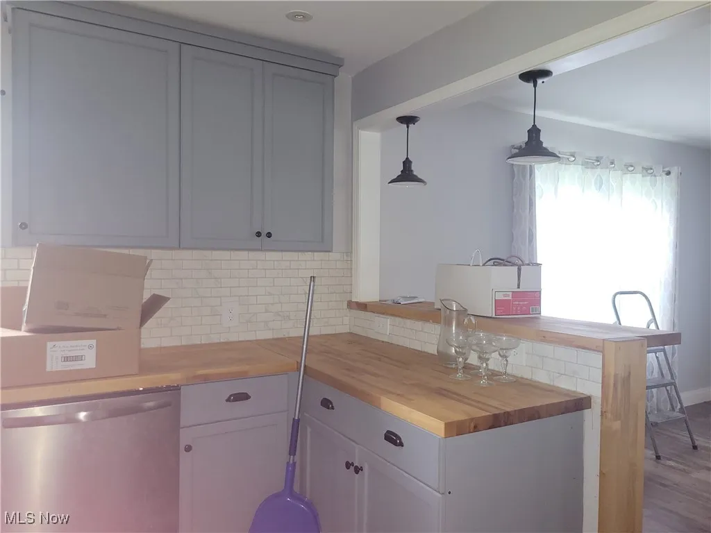 Kitchen featuring stainless steel dishwasher, decorative backsplash, pendant lighting, butcher block counters, and a peninsula