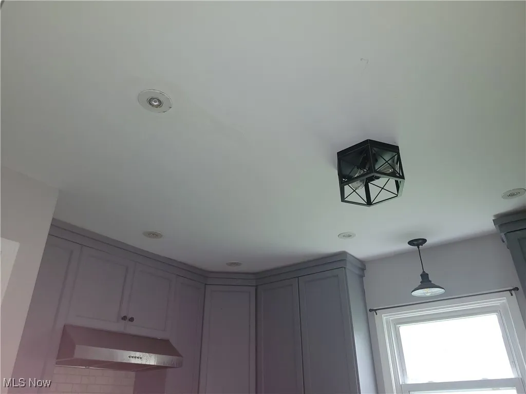 Room details with under cabinet range hood, gray cabinetry, and hanging light fixtures