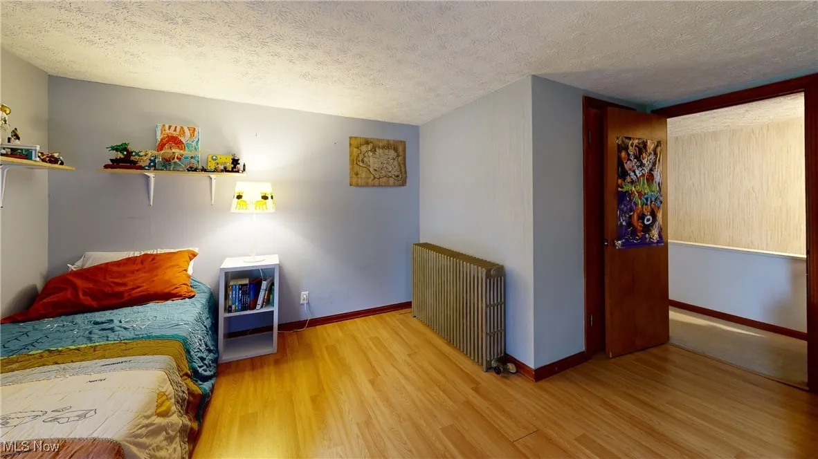 Bedroom with a textured ceiling, wood finished floors, baseboards, and radiator