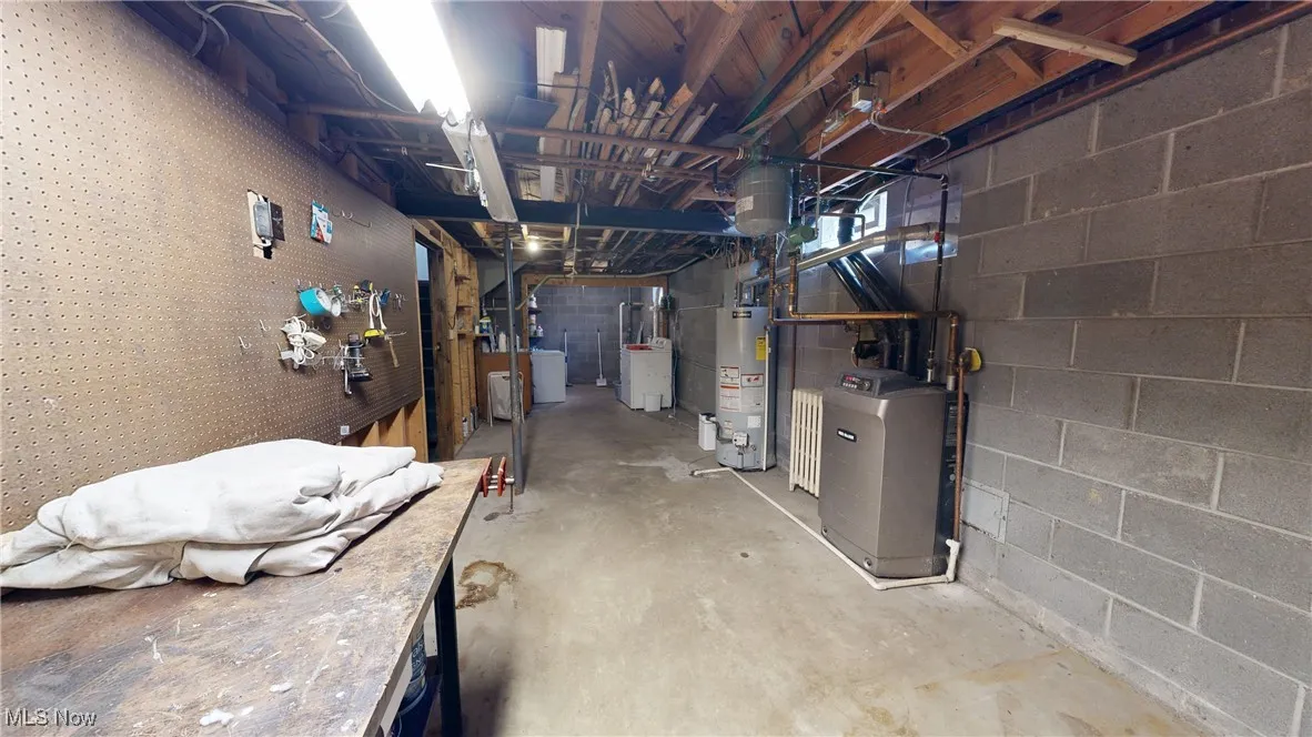 Unfinished below grade area featuring gas water heater, washer / dryer, and concrete block wall