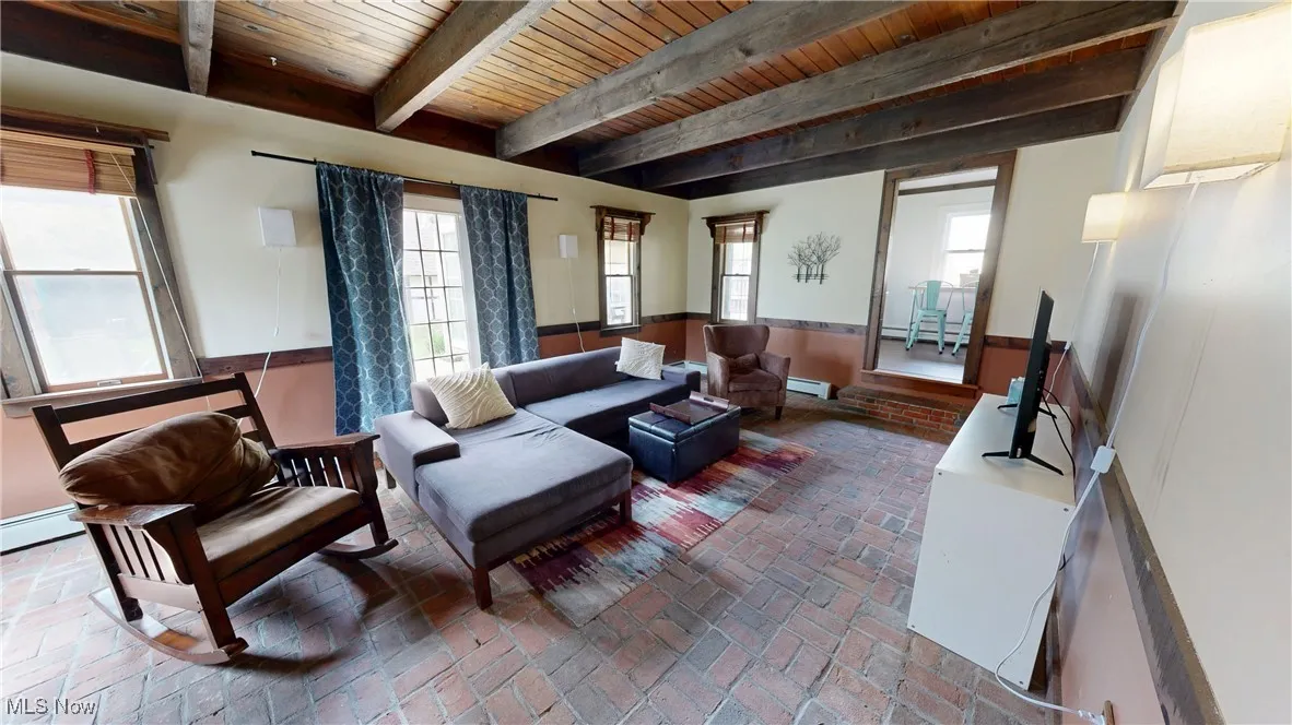 Living room featuring a baseboard heating unit, wooden ceiling, brick floor, and beam ceiling