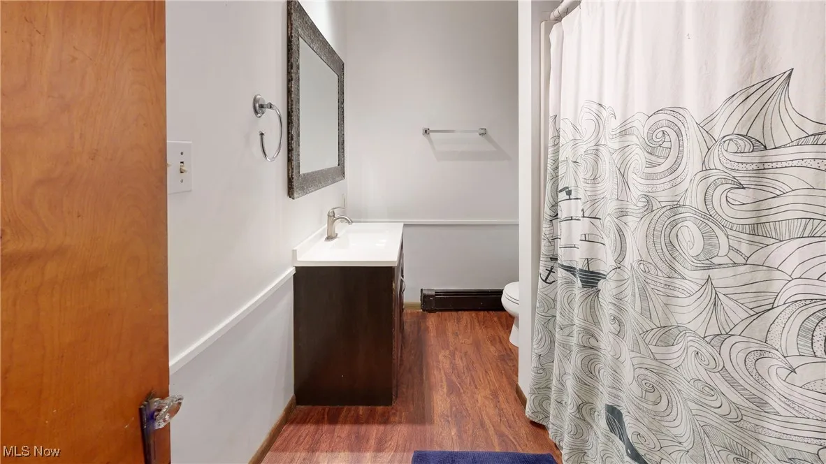 Full bathroom featuring wood finished floors, baseboard heating, toilet, vanity, and curtained shower