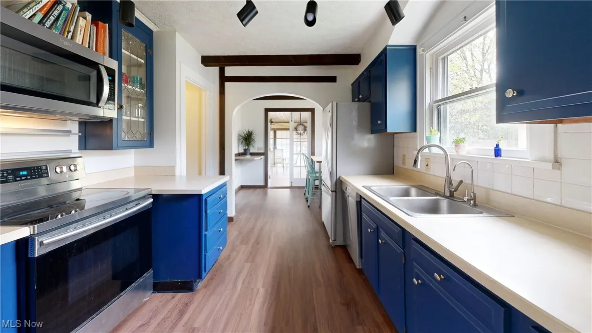 Kitchen with a sink, appliances with stainless steel finishes, blue cabinets, arched walkways, and wood finished floors