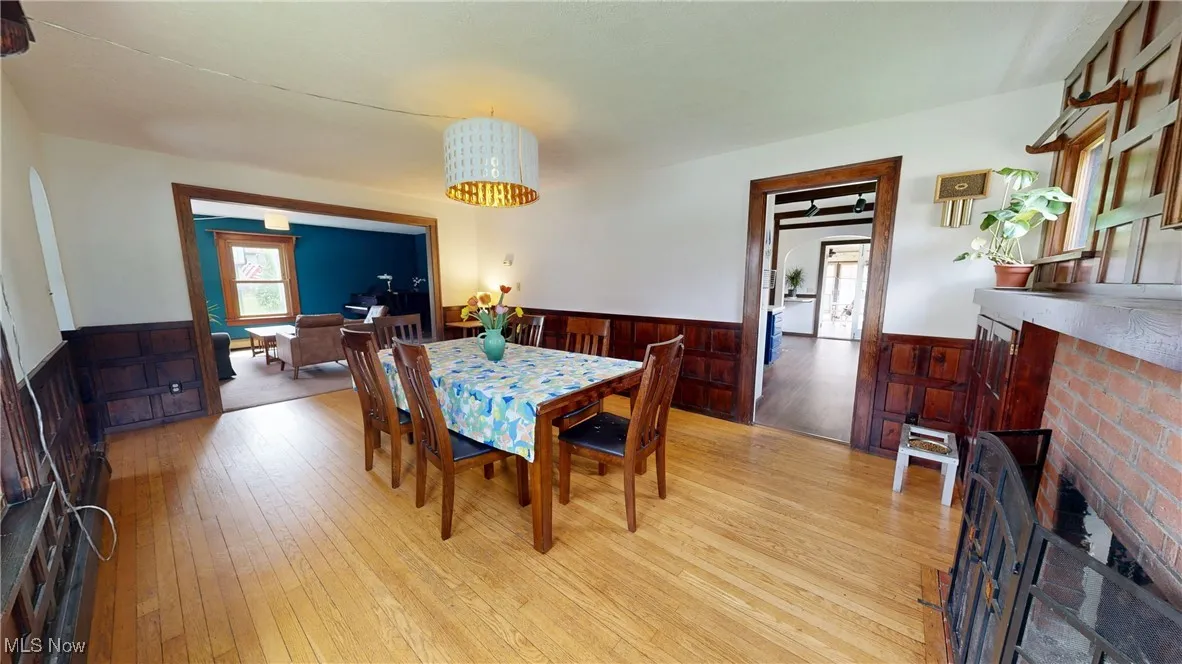 Dining room with a wainscoted wall, wooden walls, a fireplace, and light wood finished floors