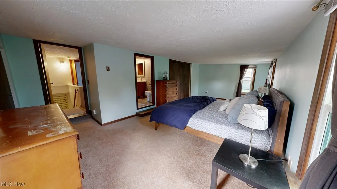 Bedroom with carpet, ensuite bath, a textured ceiling, and baseboards