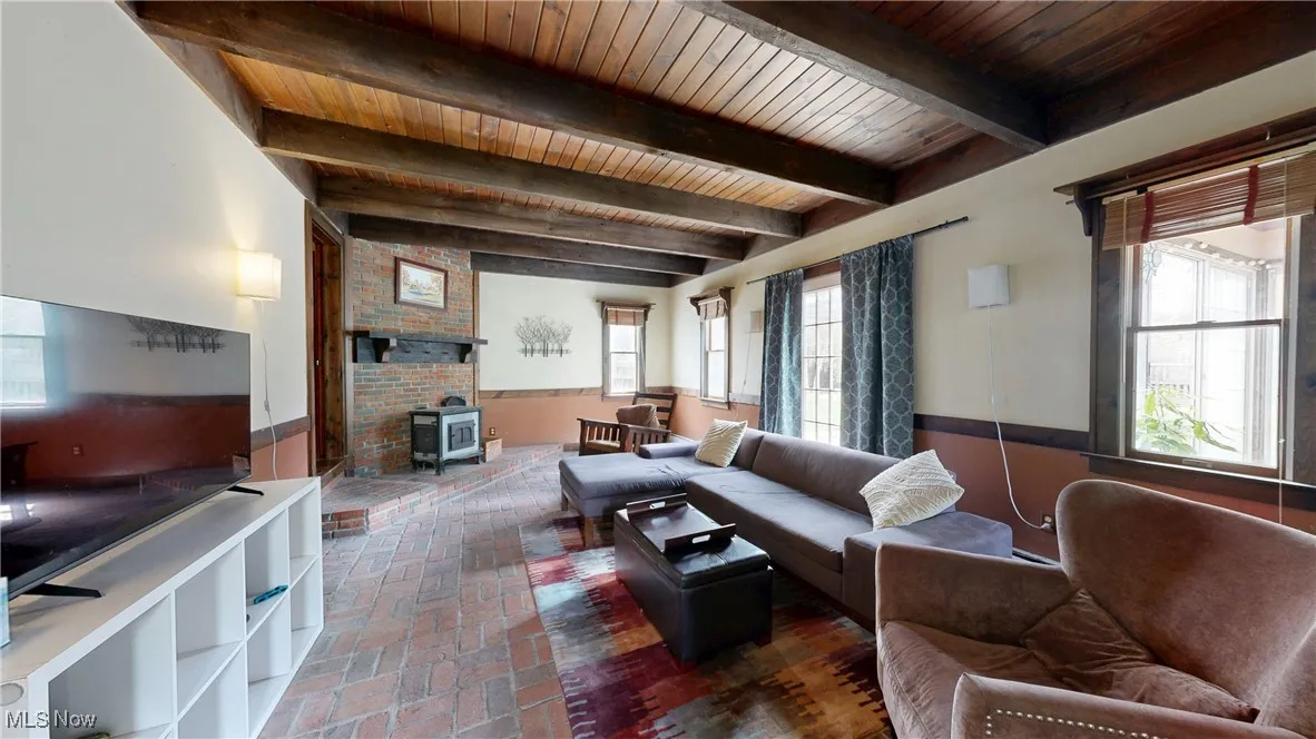 Living room with beamed ceiling, a wood stove, brick floor, and wood ceiling