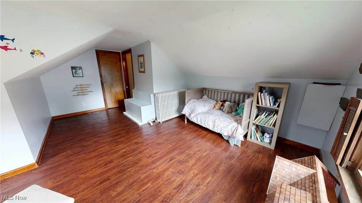 Bedroom with wood finished floors, vaulted ceiling, and baseboards