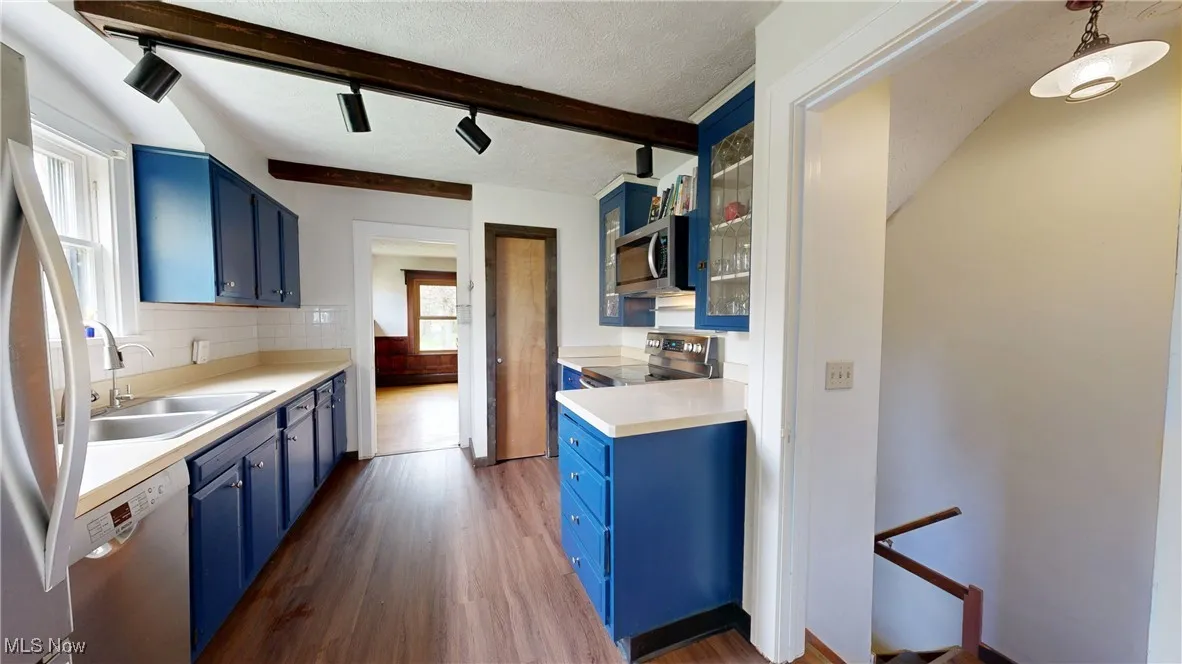 Kitchen with appliances with stainless steel finishes, dark wood-type flooring, blue cabinetry, and beamed ceiling