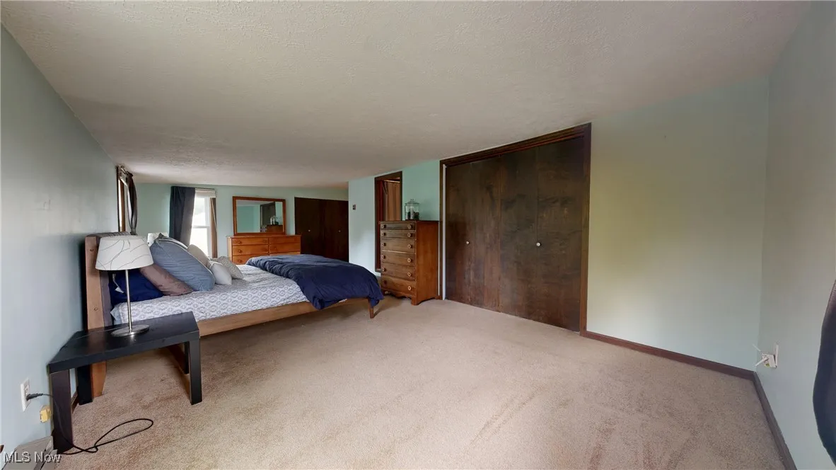 Carpeted bedroom with baseboards, a textured ceiling, and two closets