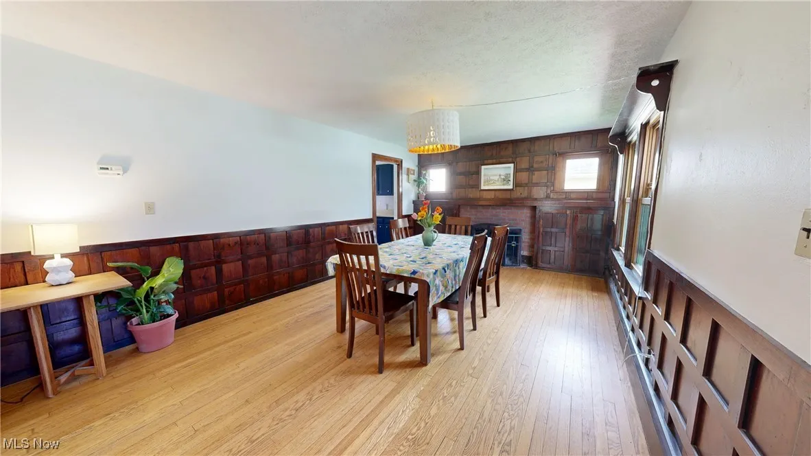 Dining space with wood walls, light wood-type flooring, a wainscoted wall, and a notable chandelier