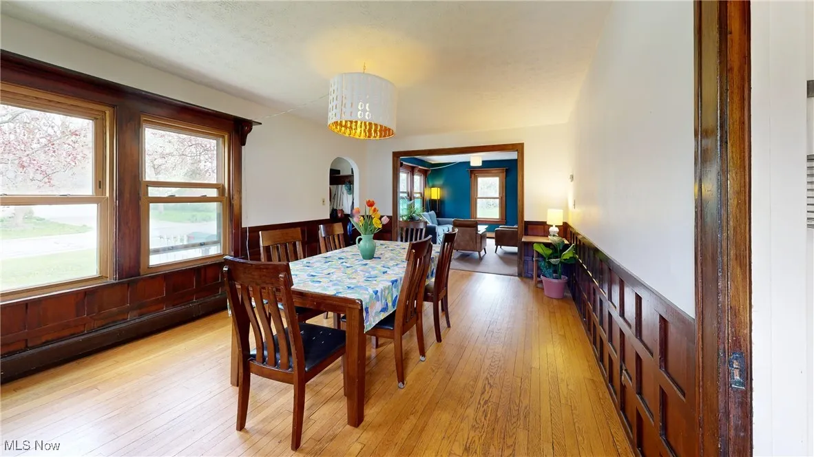 Dining area with a wainscoted wall, light wood-style flooring, and arched walkways