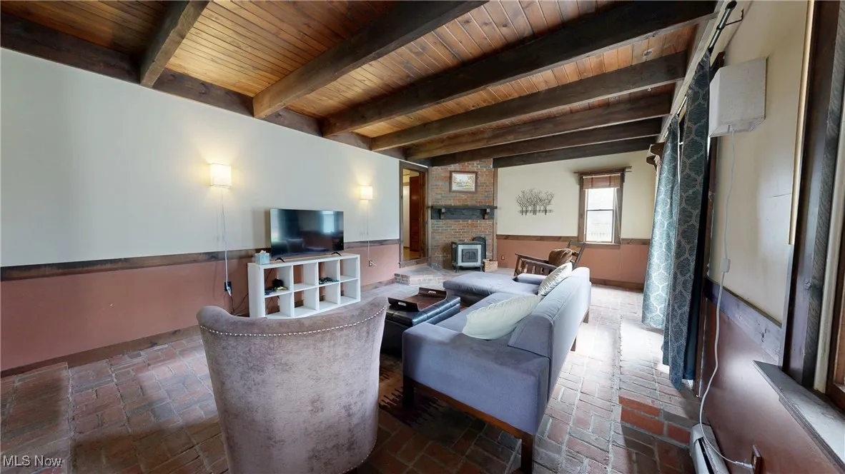 Living area with wooden ceiling, beamed ceiling, brick floor, baseboards, and a wood stove