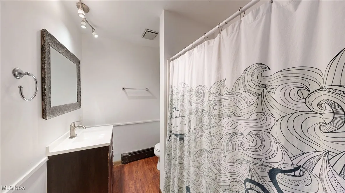 Full bathroom with wood finished floors, baseboard heating, toilet, vanity, and visible vents