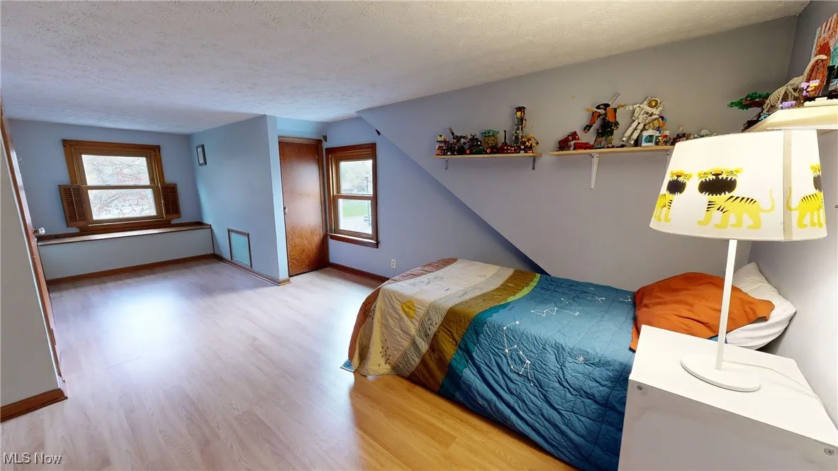 Bedroom featuring a textured ceiling, multiple windows, wood finished floors, and baseboards