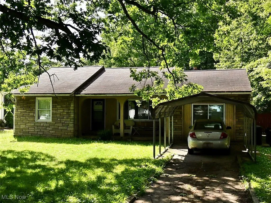 Ranch-style home with roof with shingles, stone siding, a front yard, covered porch, and driveway