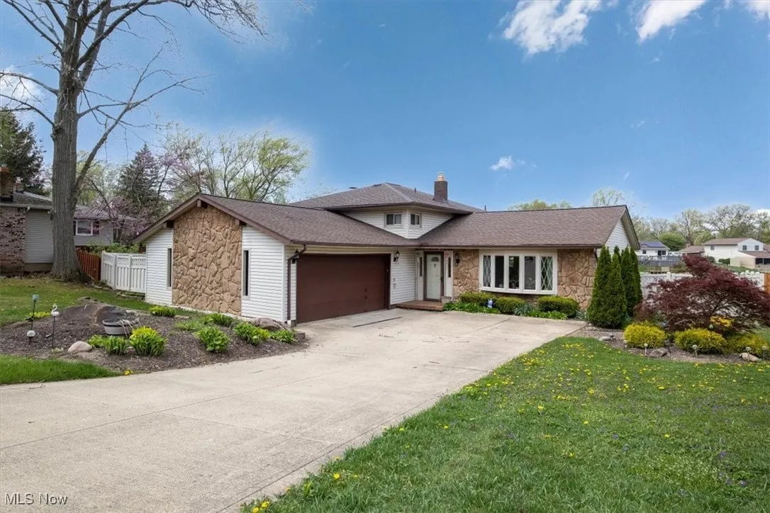 View of front facade with concrete driveway, an attached garage, a chimney, and stone siding