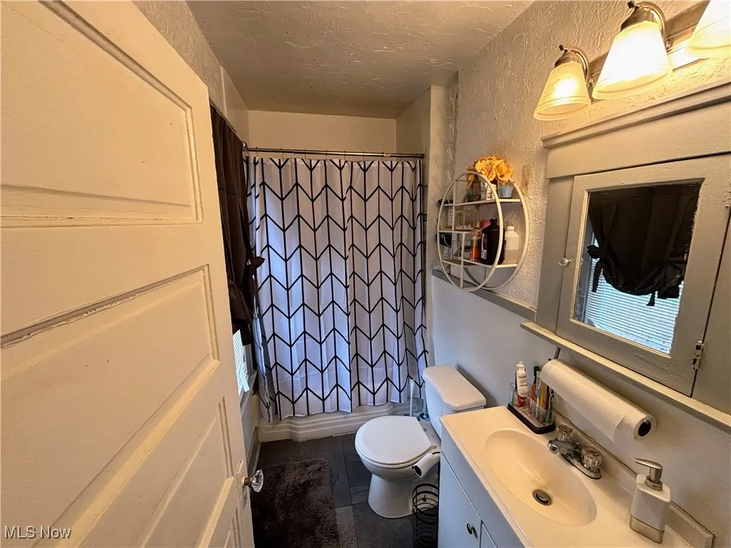 Bathroom featuring a textured wall, vanity, a textured ceiling, tile patterned flooring, and shower / tub combo with curtain