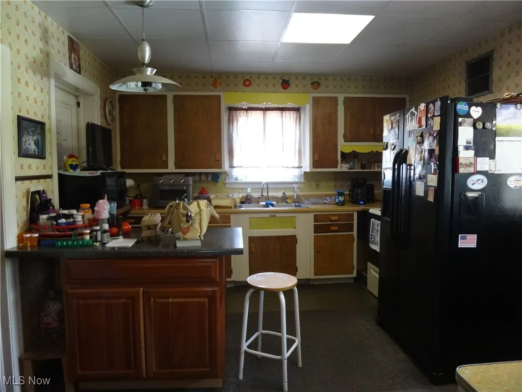 Kitchen featuring a sink, a movable island, black fridge with ice dispenser, and wallpapered walls
