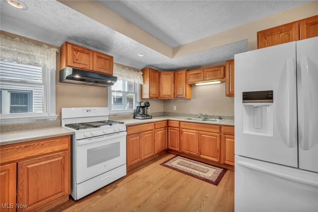 Kitchen featuring a textured ceiling, light countertops, light wood finished floors, under cabinet range hood, and white appliances