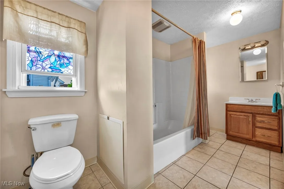 Full bathroom featuring toilet, a textured ceiling, tile patterned flooring, and vanity