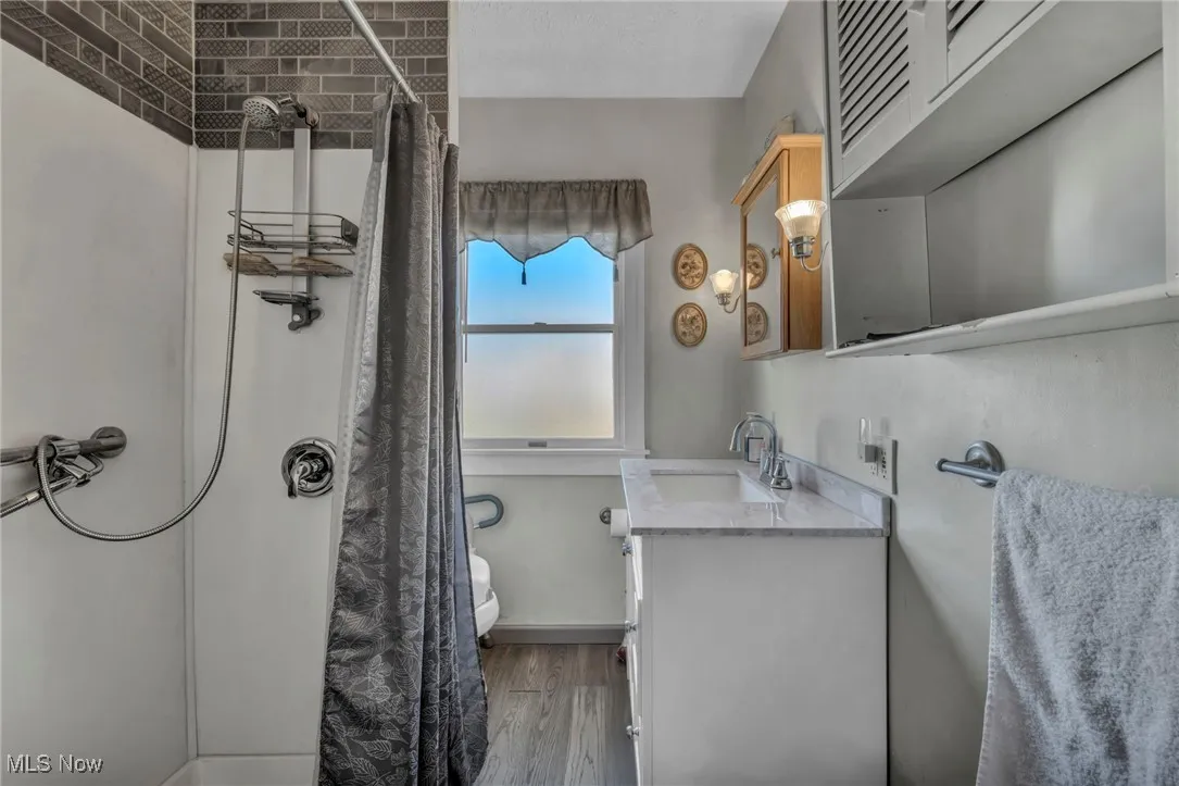 Full bath with vanity, curtained shower, toilet, and wood finished floors