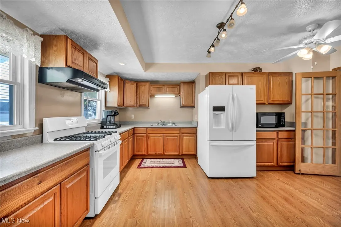 Kitchen featuring brown cabinets, a sink, white appliances, light wood-type flooring, and under cabinet range hood