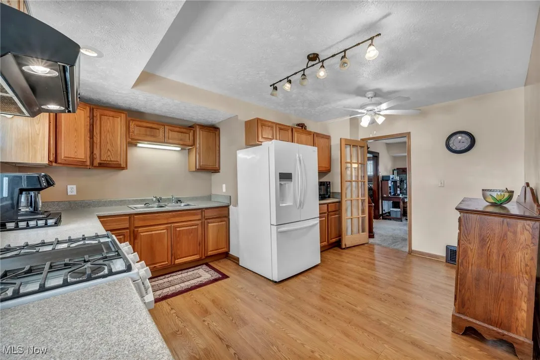 Kitchen with a sink, a textured ceiling, range hood, and white appliances