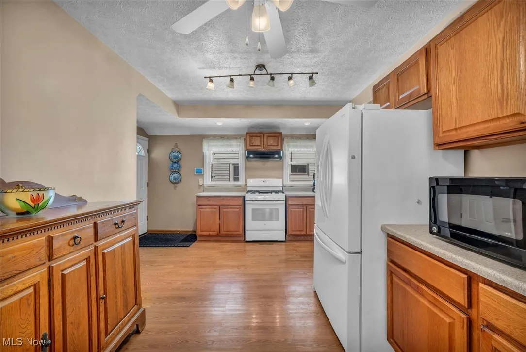 Kitchen with brown cabinets, under cabinet range hood, white appliances, and light wood-style flooring