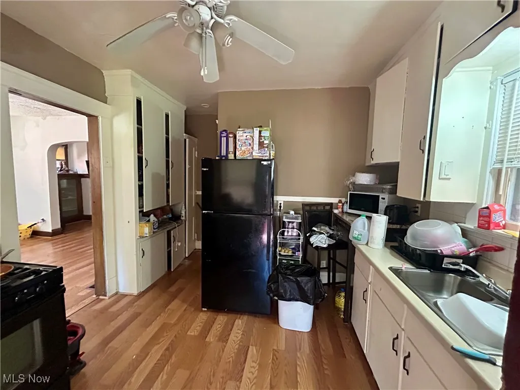 Kitchen featuring white cabinets, a sink, light wood-style flooring, a ceiling fan, and black appliances