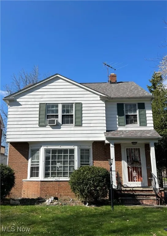 Traditional home featuring brick siding, a front lawn, roof with shingles, and a chimney