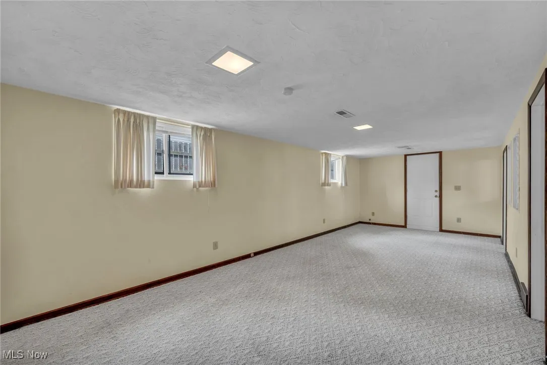 Below grade area with baseboards, a textured ceiling, visible vents, and light colored carpet