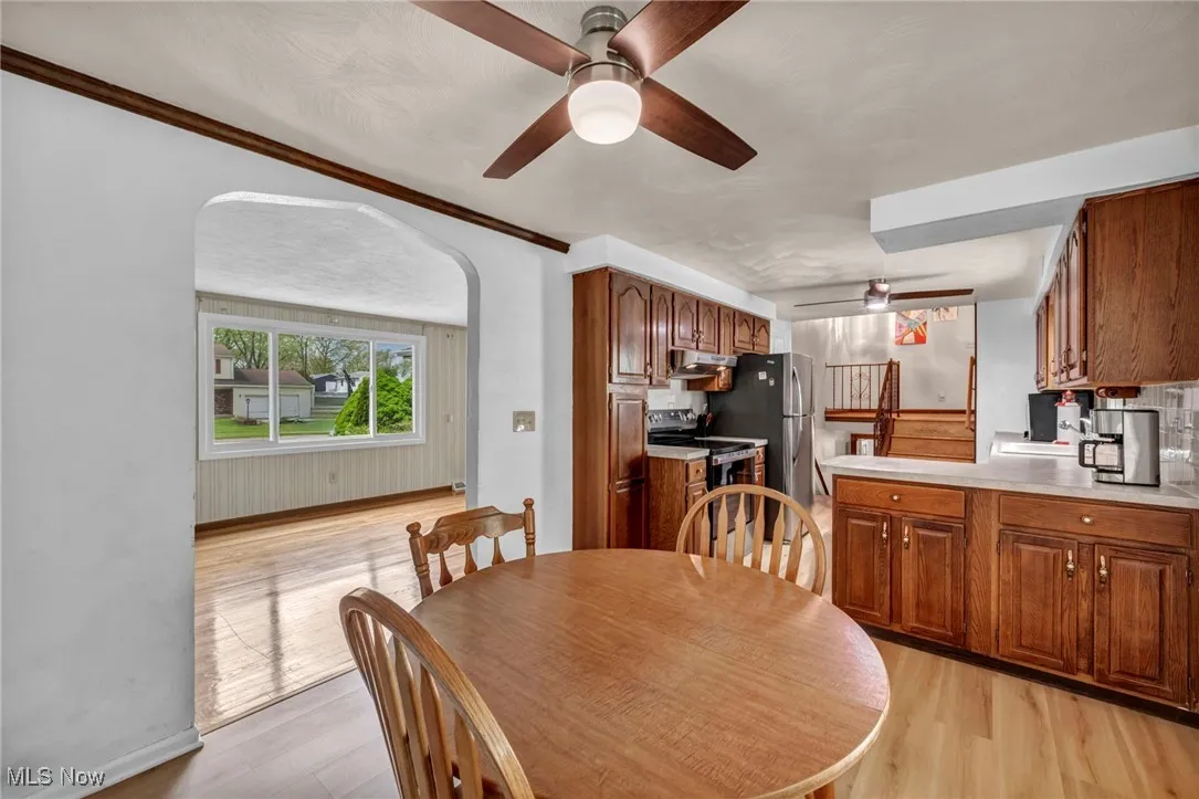 Dining room with light wood-style floors, arched walkways, baseboards, and ceiling fan