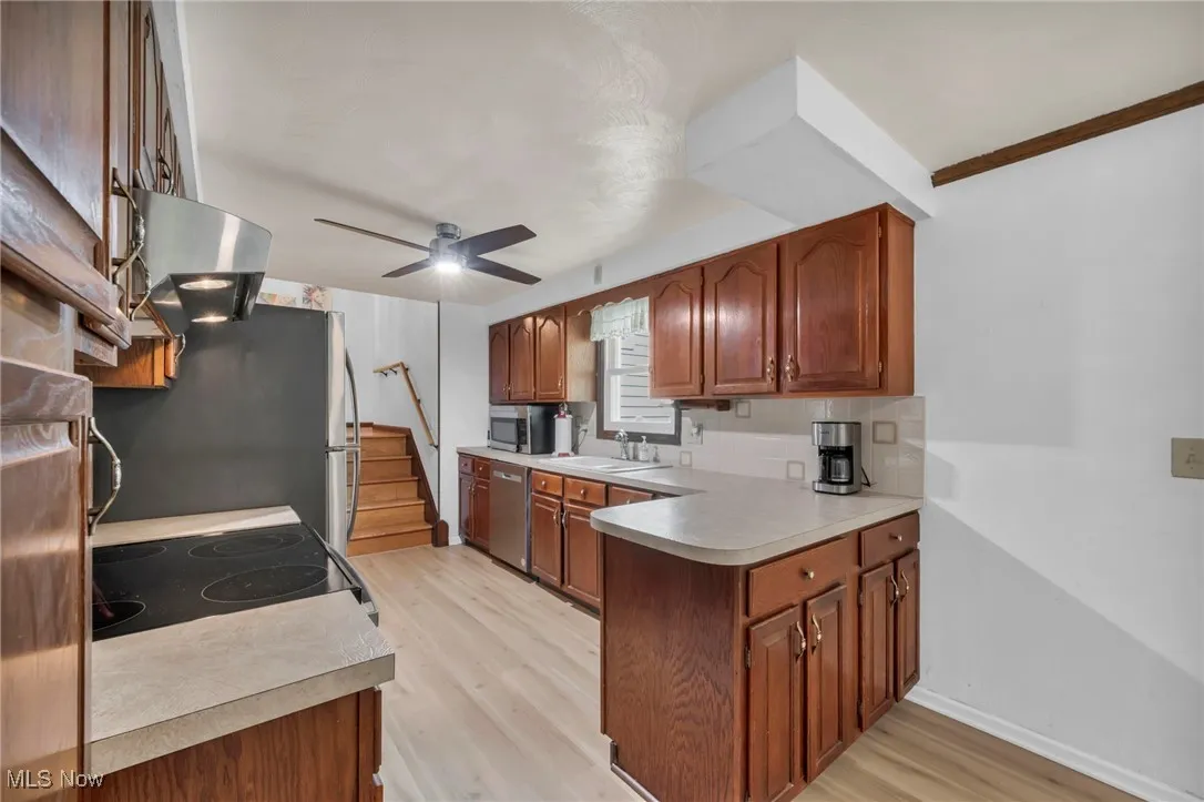 Kitchen featuring a sink, a peninsula, a ceiling fan, light wood-style flooring, and stainless steel appliances