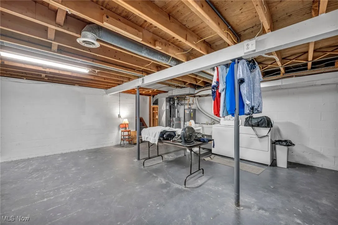 Unfinished basement with water heater, concrete block wall, and independent washer and dryer